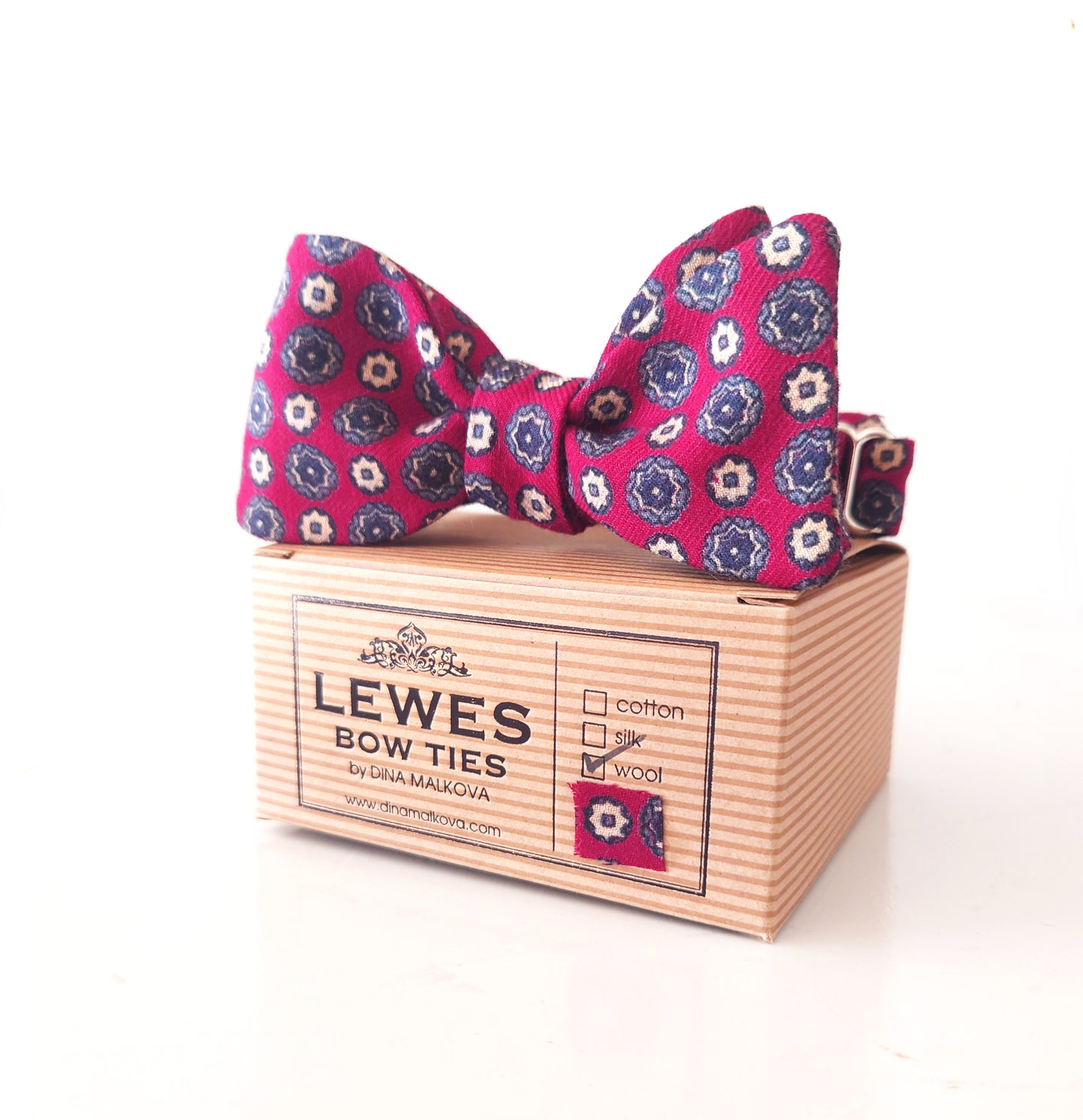 Pink floral bow tie on a wooden box with 'Lewes Bow Ties' branding by lewesbowties.co.uk
