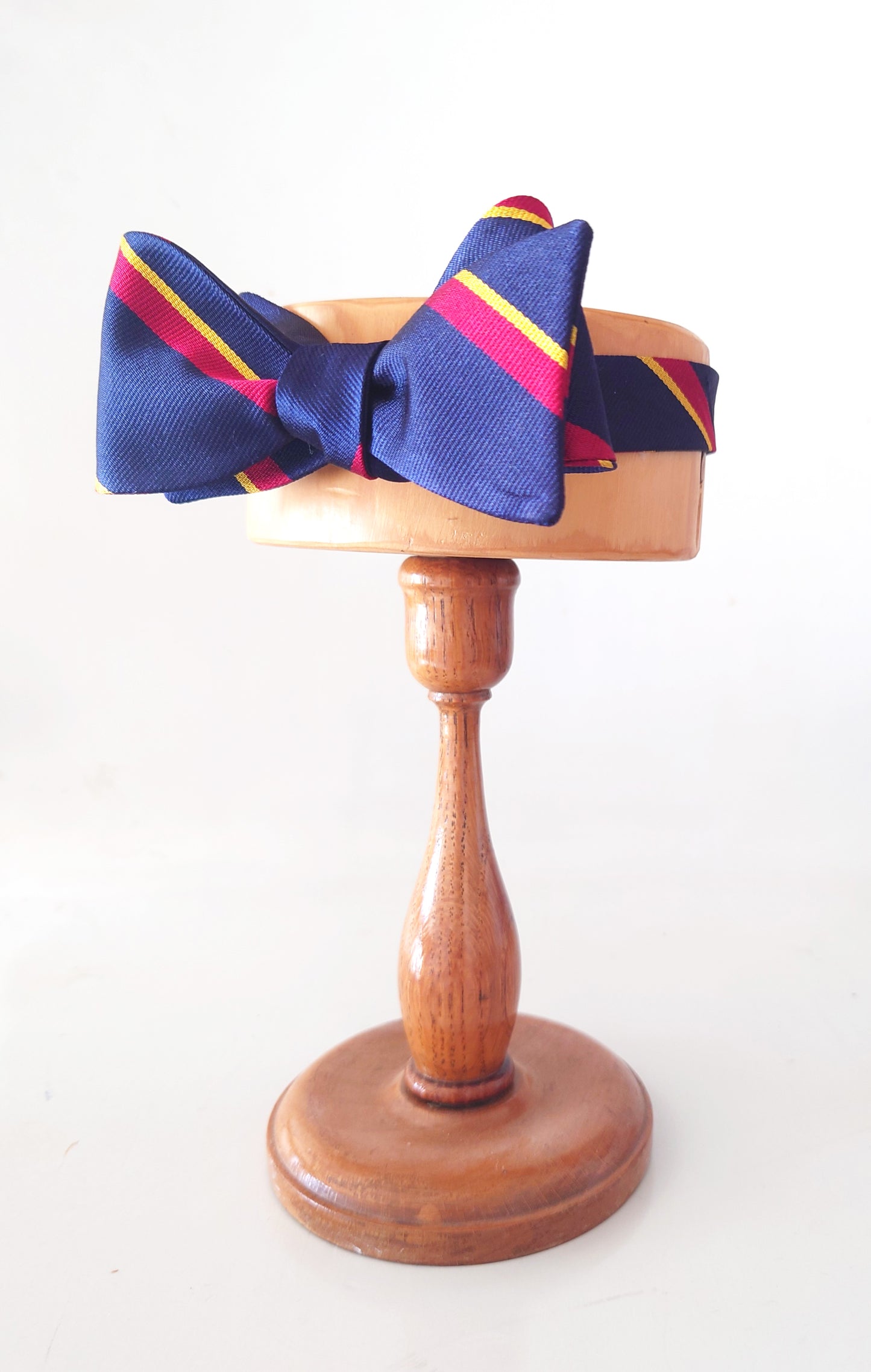 Blue bow tie with red and yellow stripes on a wooden stand against a white background