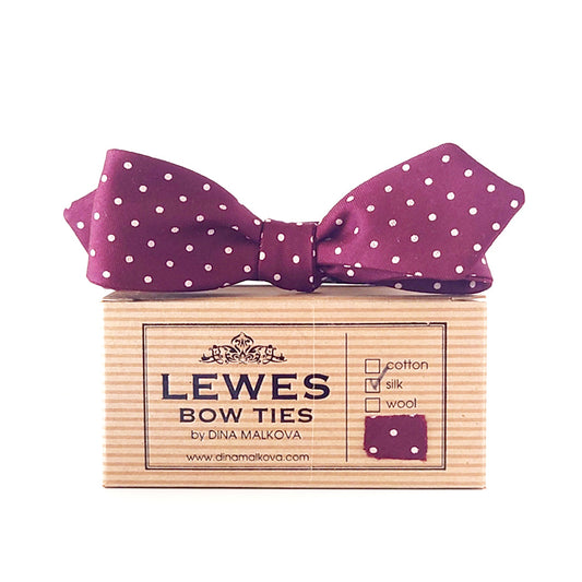 A burgundy silk bow tie with white polka dots, presented on top  'LEWES BOW TIES box