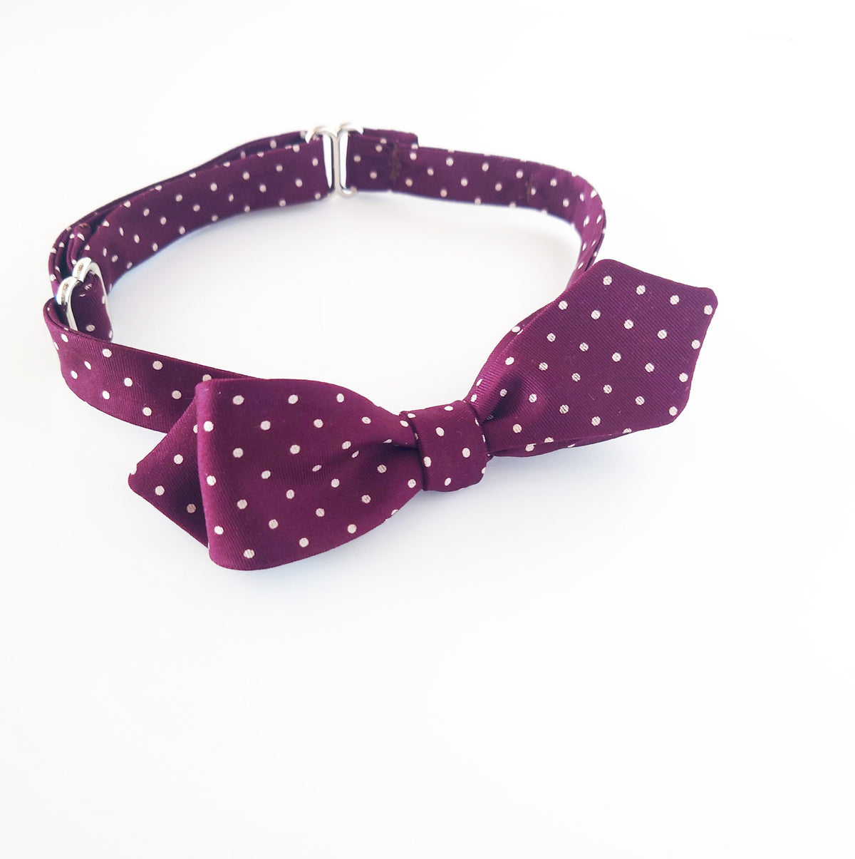 A burgundy fabric bow tie with small white polka dots, displayed on a clean white background.