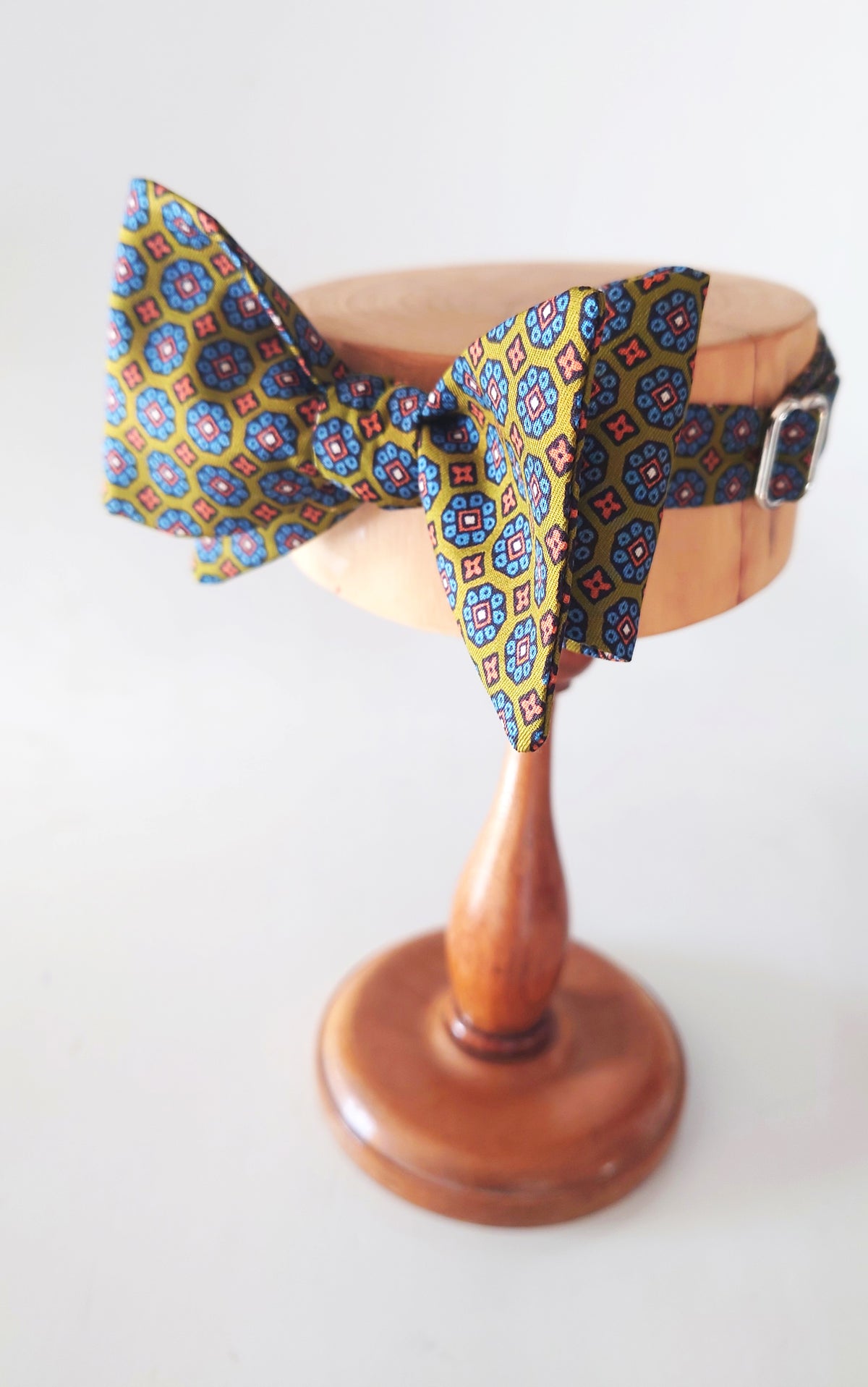 A patterned bow tie with a geometric medallion design in yellow, blue, red, and black, displayed by Lewes Bow Ties
