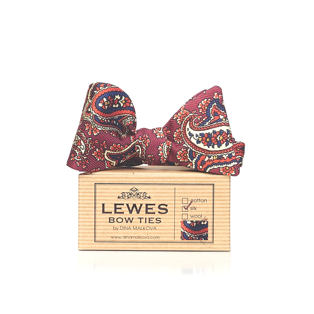 A paisley patterned bow tie in orange, navy, cream 100% silk fabric, displayed on top of a Lewes Bow Ties brand box. 