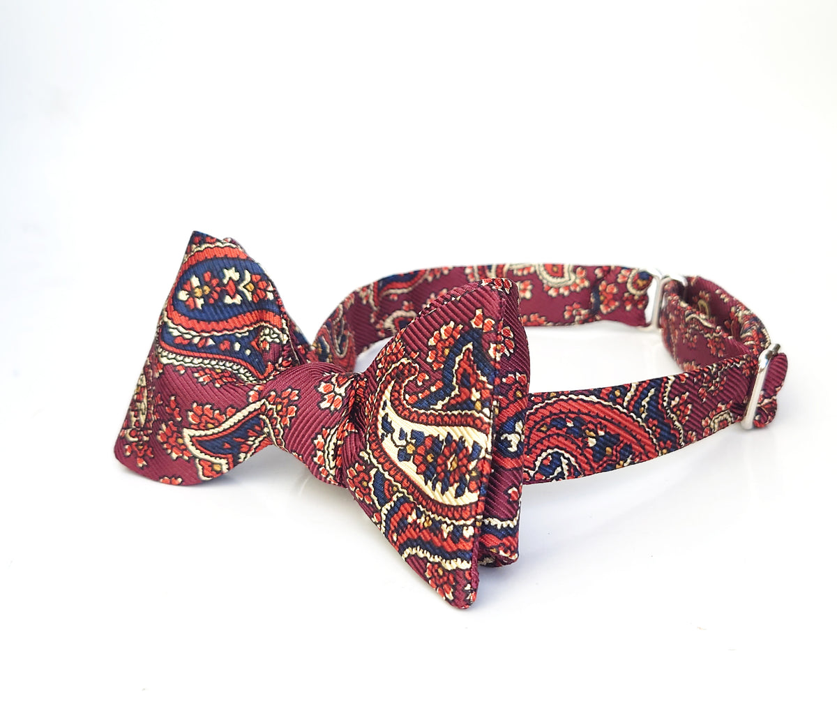 A self tie bow tie with a detailed paisley pattern in orange, navy blue, and cream, displayed on a clean white background.