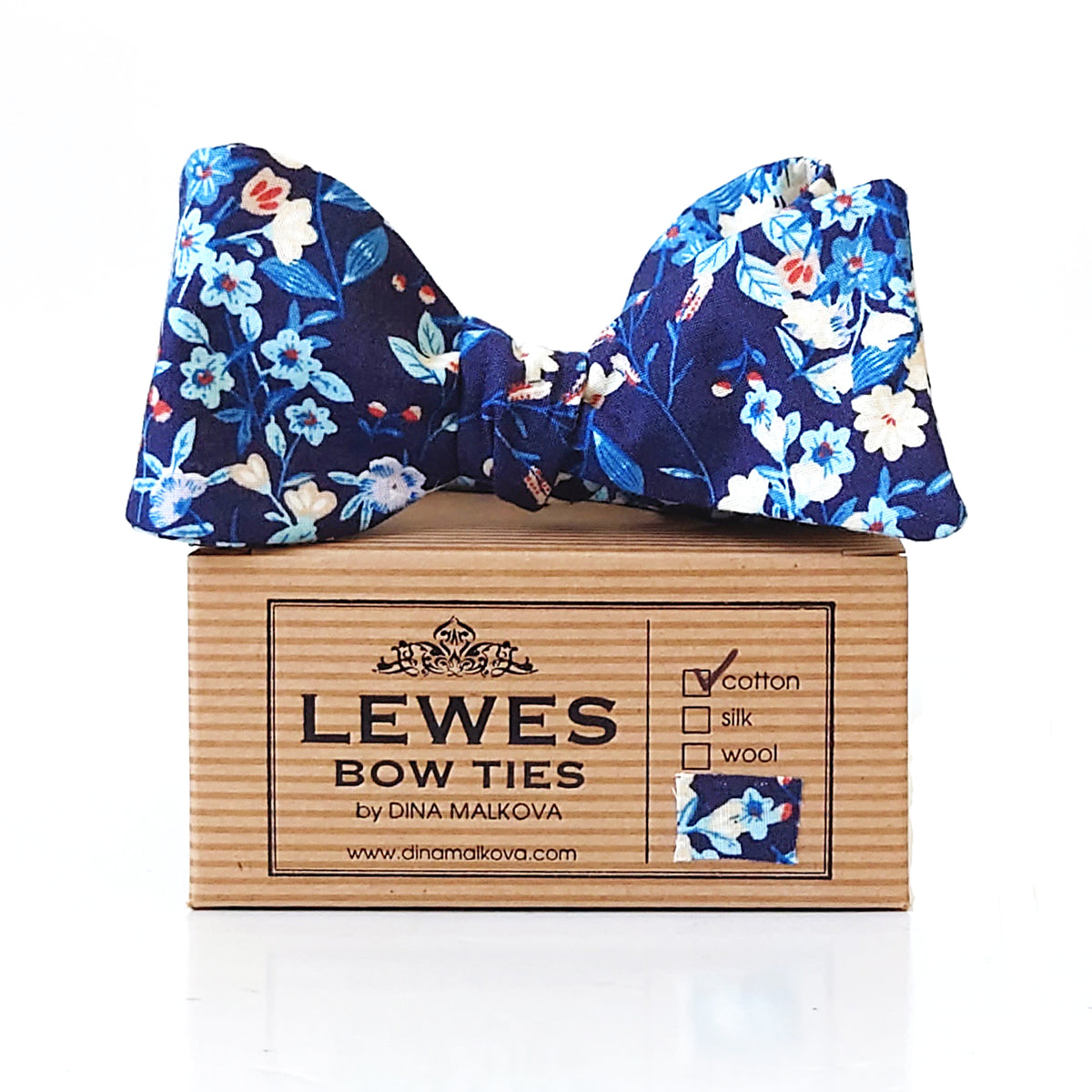 A navy blue floral bow tie with blue, white, and light blue flowers, displayed on top of Lewes Bow Ties box.