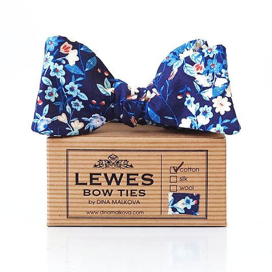 A navy blue floral bow tie with blue, white, and light blue flowers, displayed on top of Lewes Bow Ties box.